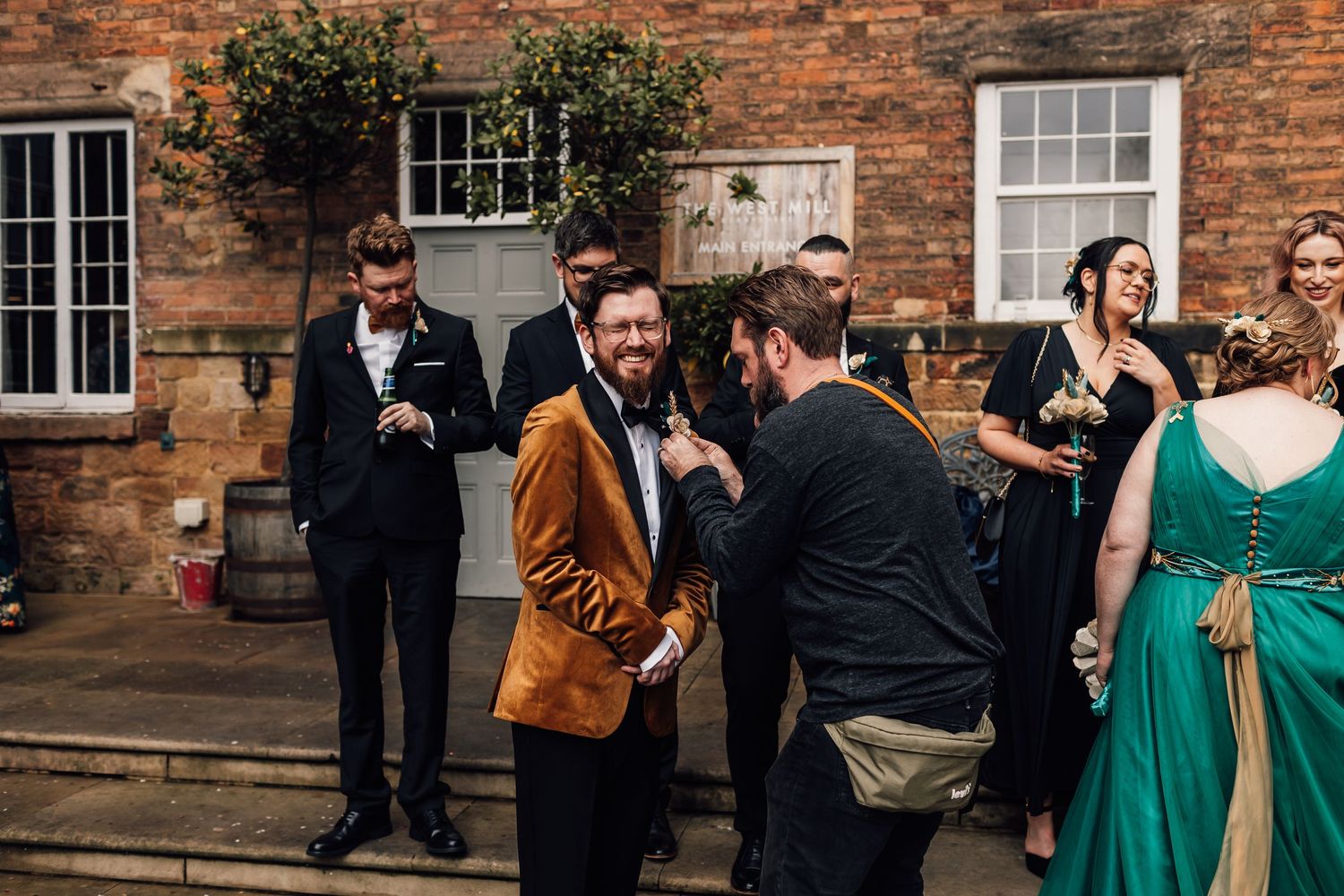 Wedding guests mingle and socialize outside a rustic brick building during an outdoor reception.