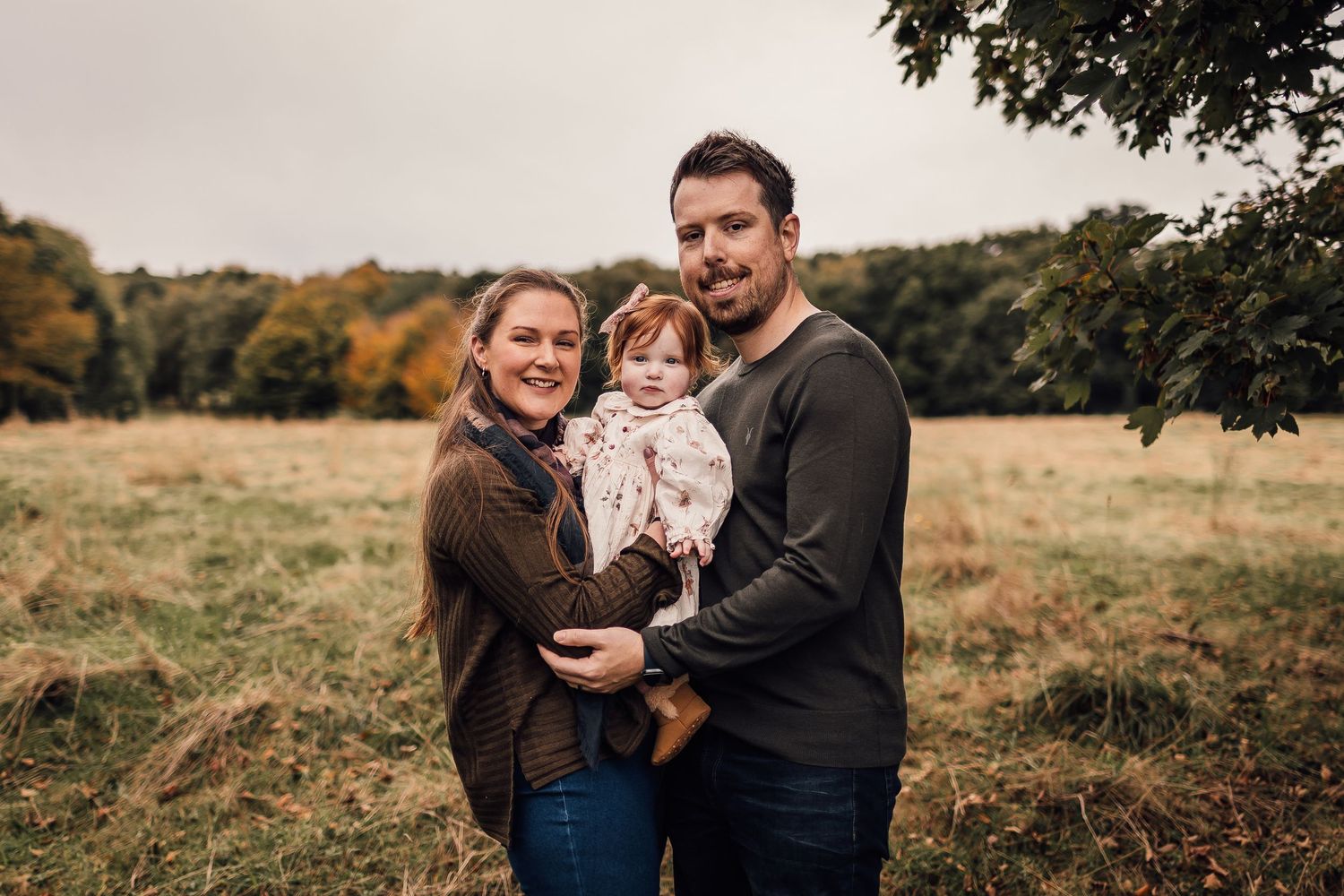 A family enjoys an autumn day together in a field with fall foliage visible in the background.