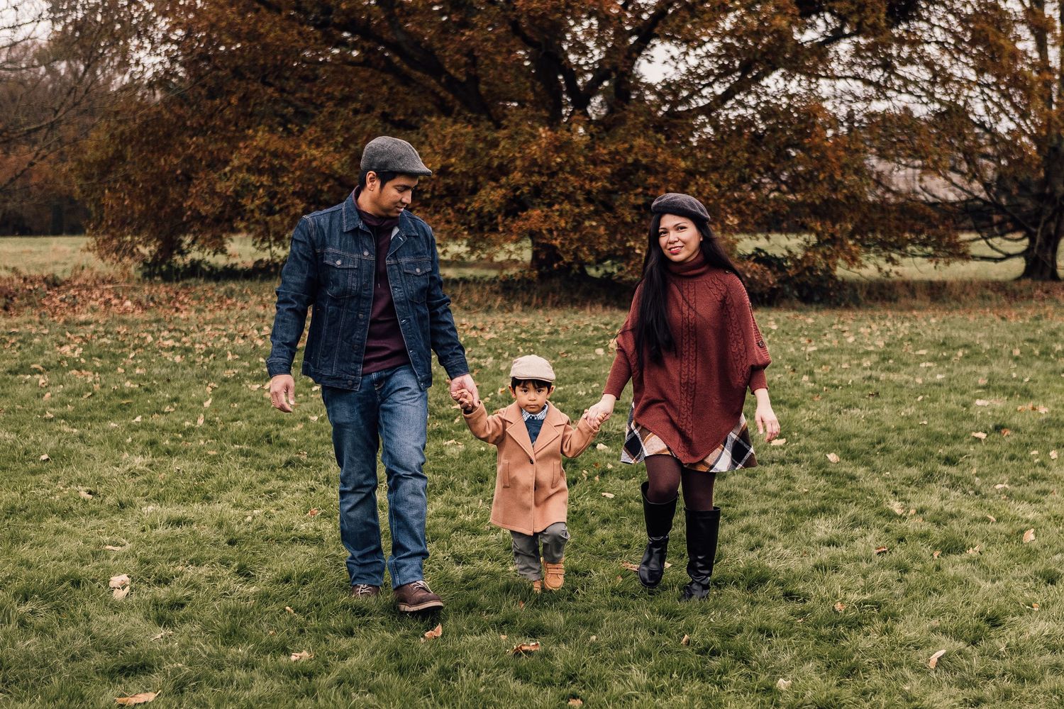 A family enjoys a walk together on grassy field during autumn with brown trees in the background.