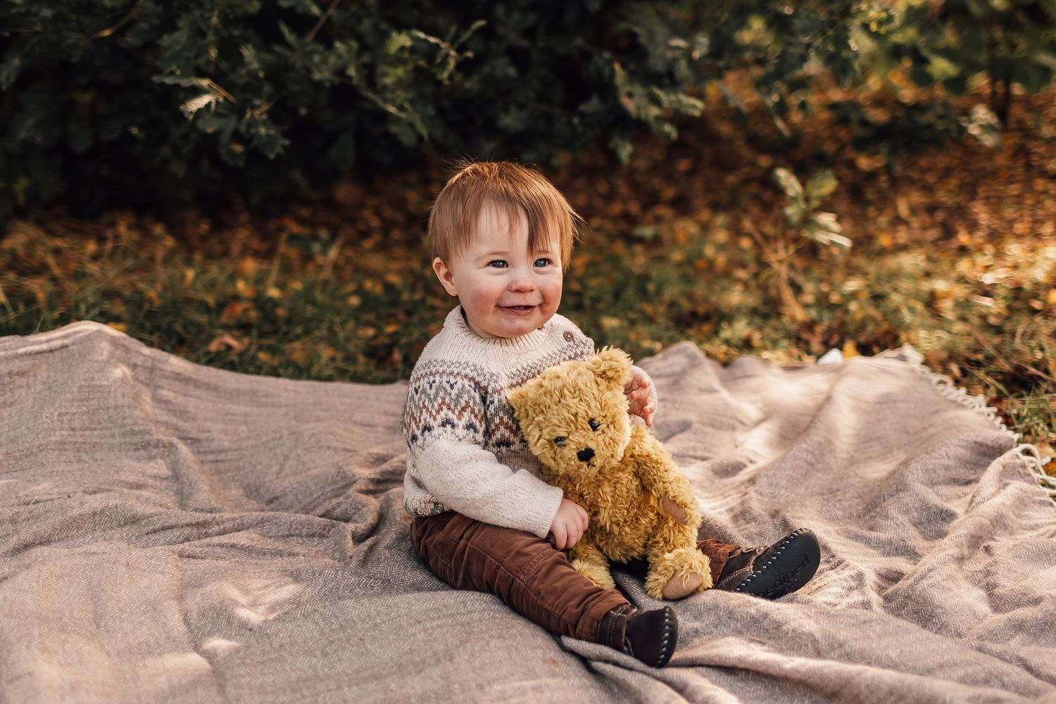 Sweet photos taken outdoors during autumn of a toddler sitting on a blanket with a stuffed bear toy.