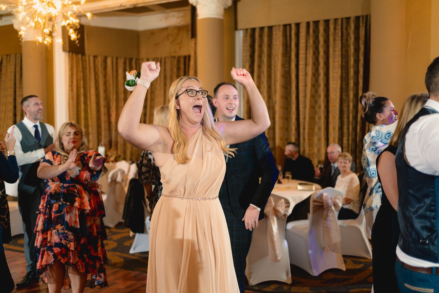 Guest in peach dress dancing enthusiastically at wedding reception.