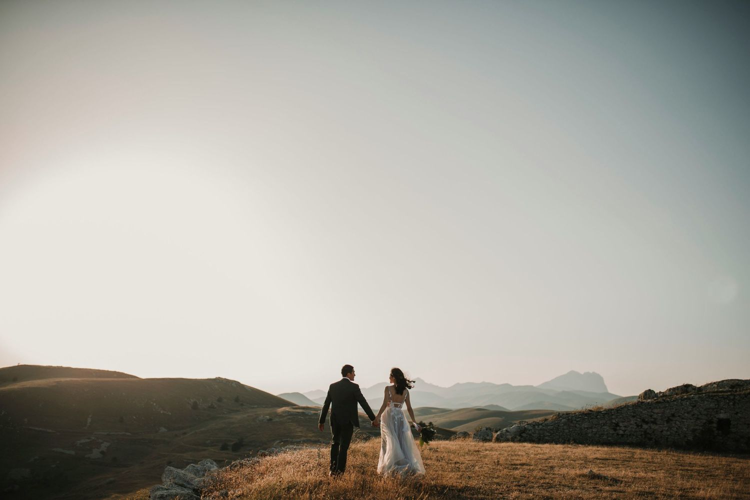 Two silhouettes walk hand in hand on a hilltop during golden hour.