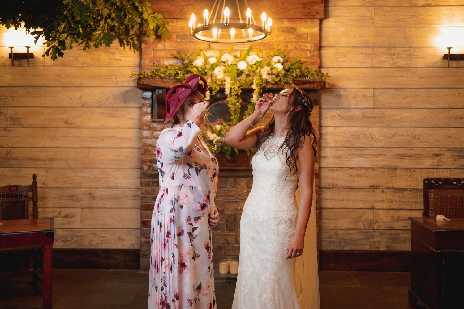 Wedding dress preparation moment in rustic wooden venue with chandelier lighting.