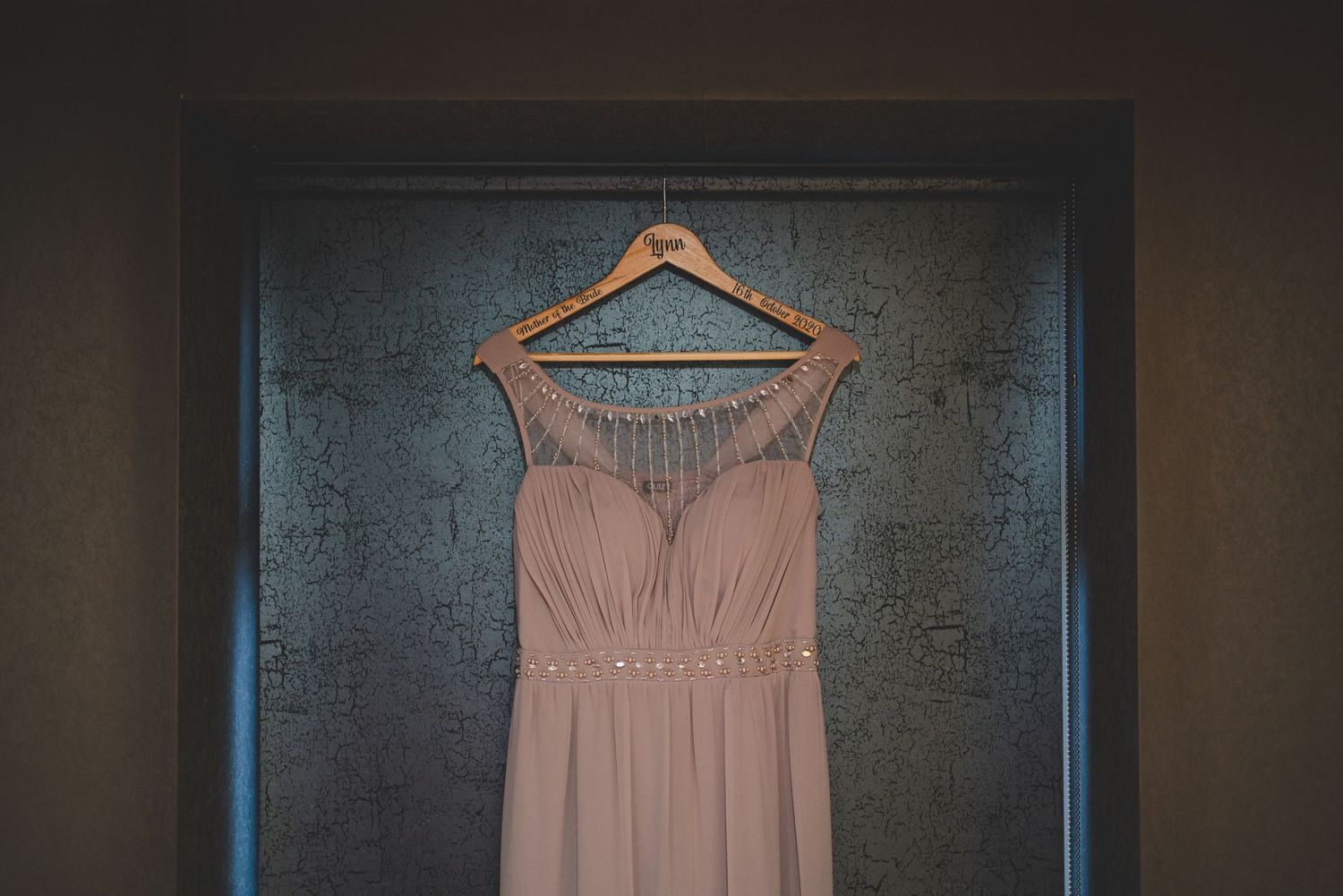 Pink satin bridesmaid dresses hanging on wooden hangers in a dimly lit closet.