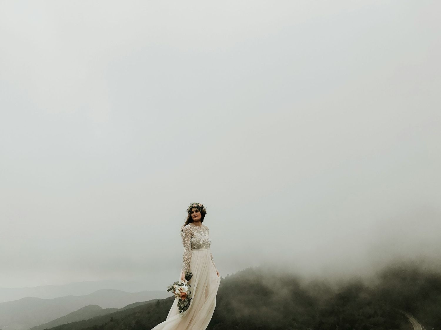 A figure in flowing white dress stands dramatically on a misty mountaintop.