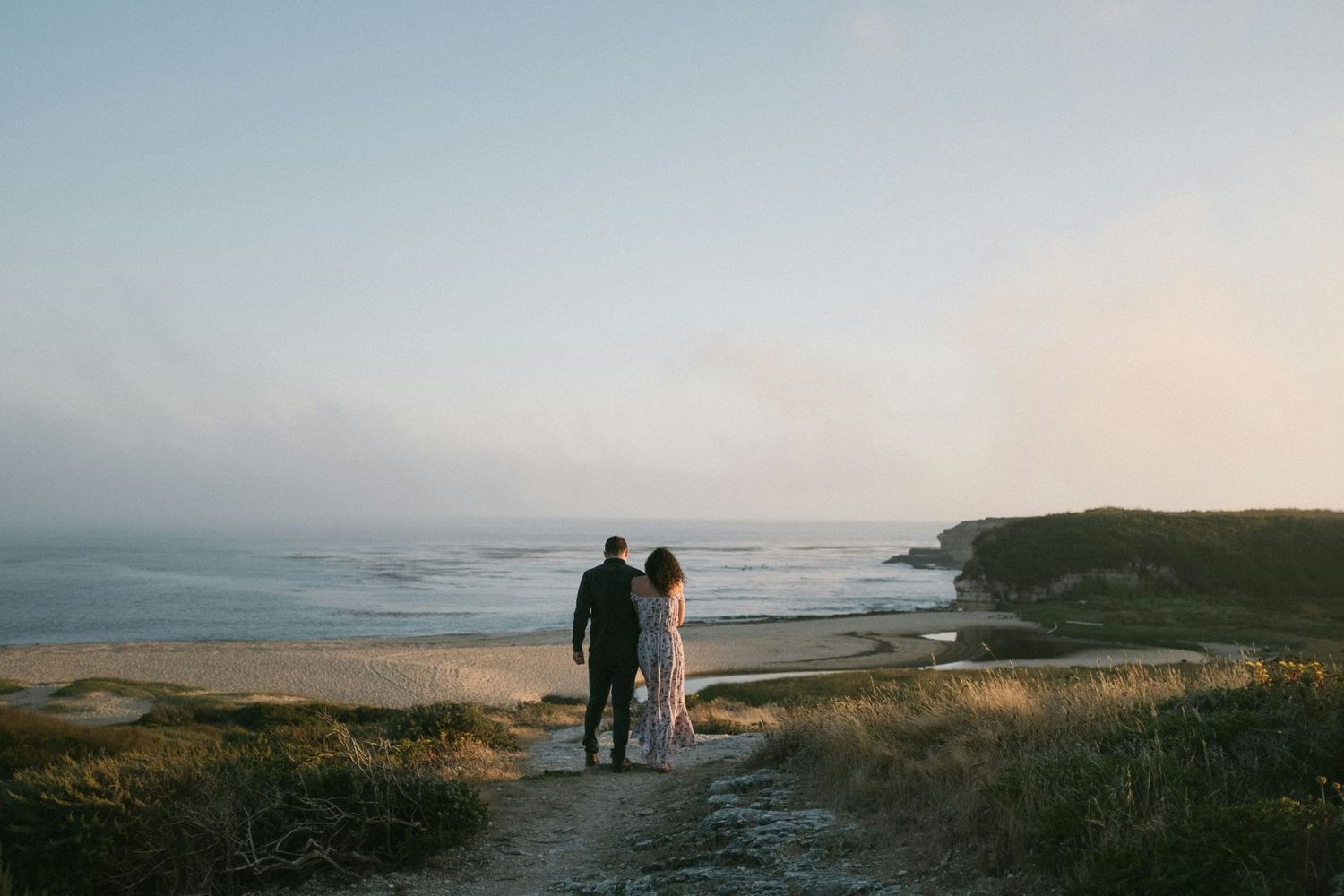 A couple overlooks a misty coastal landscape on a scenic trail.