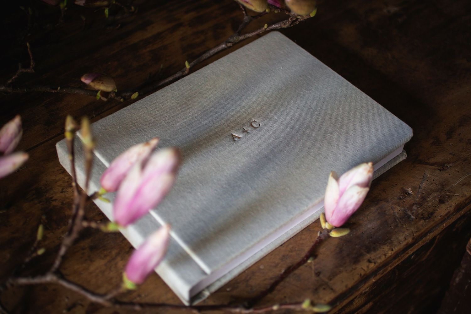 Gray book with soft pink magnolia blossoms on dark wooden surface.