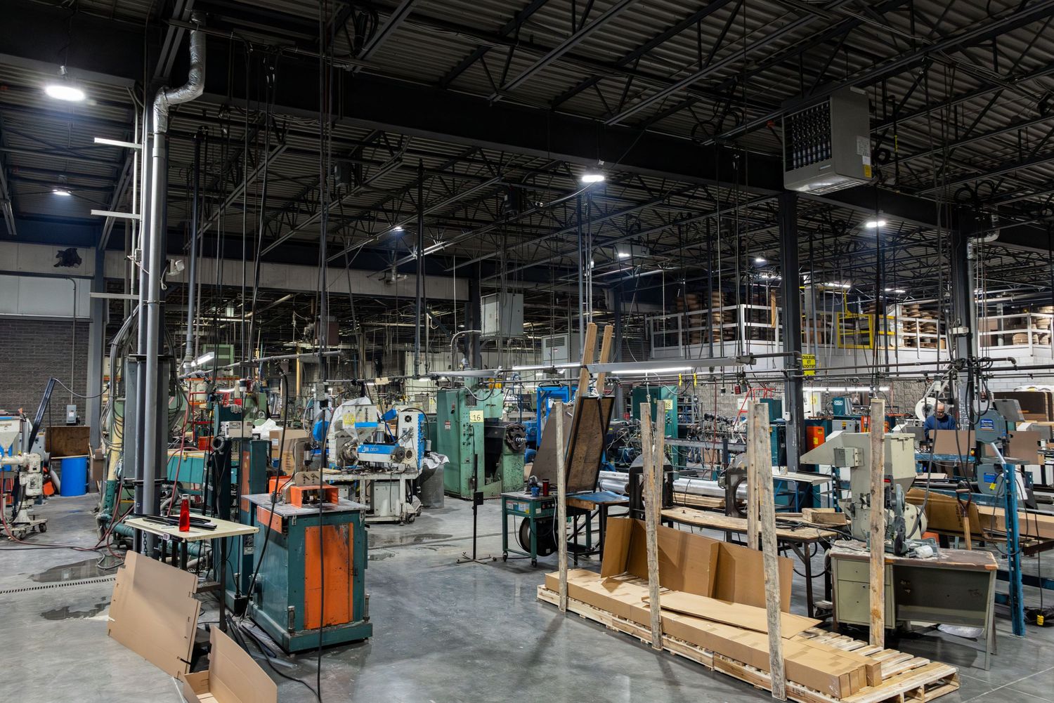 Interior view of a large manufacturing facility with work stations, machinery and overhead lighting in a warehouse setting.