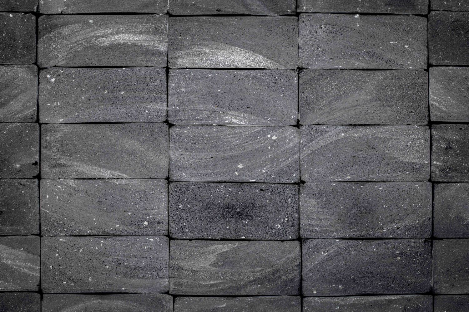 Dark gray textured stone wall with rectangular blocks arranged in a geometric pattern with subtle wavy surface details.