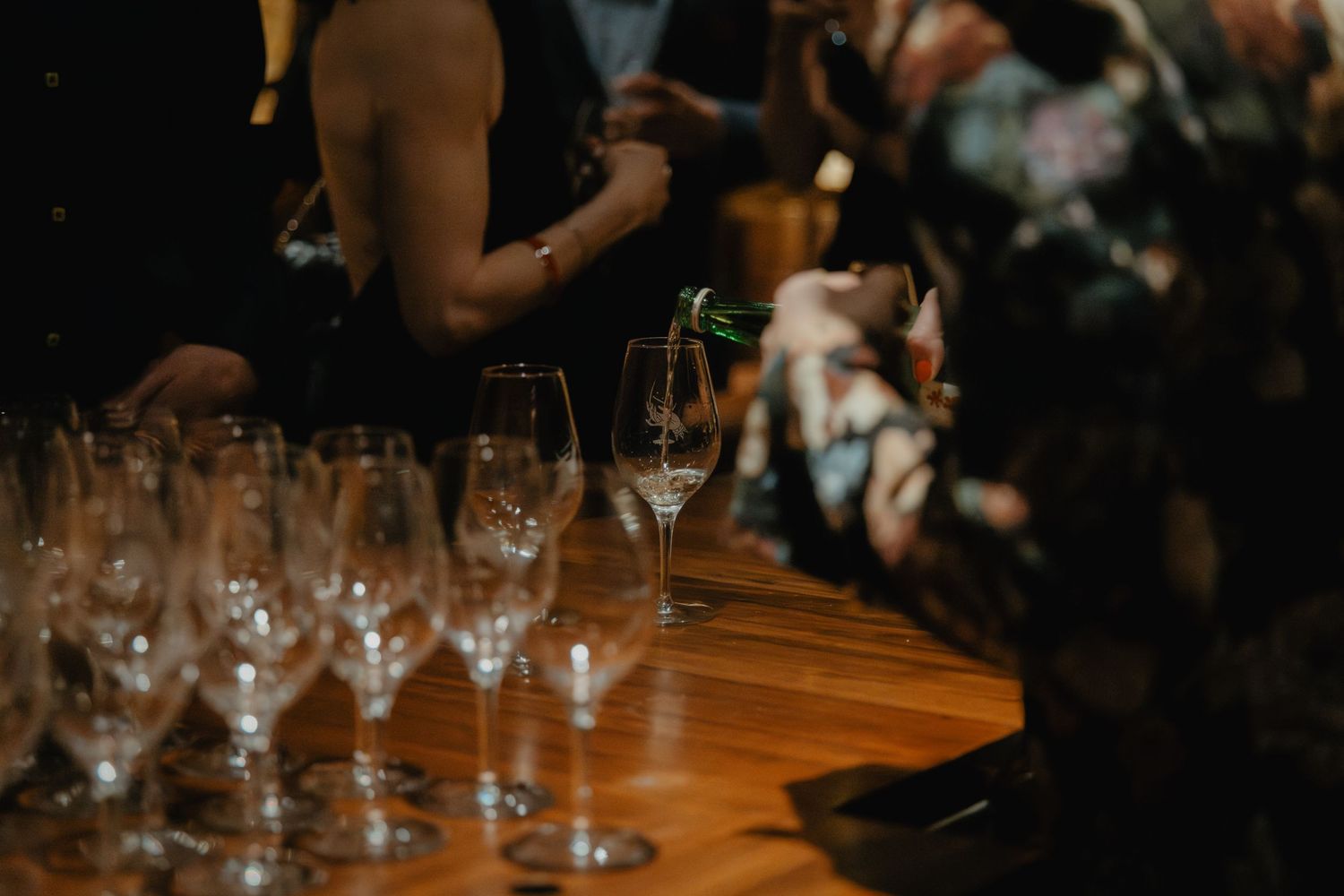 Empty wine glasses lined up on a wooden bar counter during an evening event.