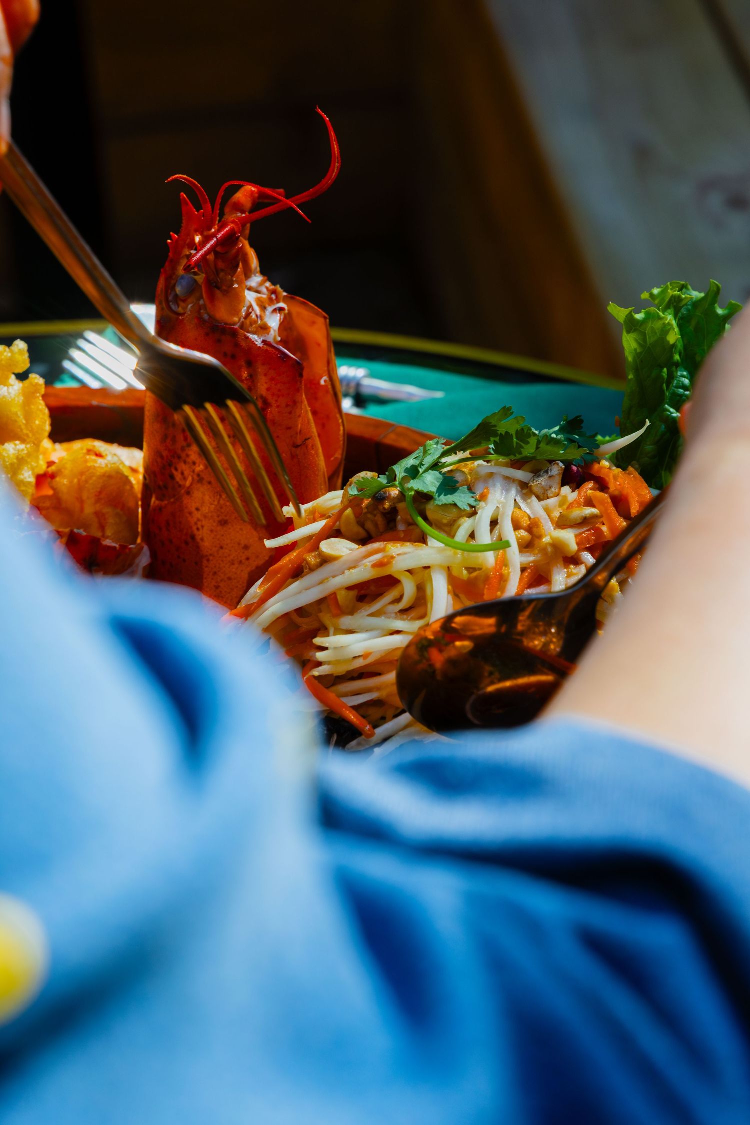 Close-up shot of a vibrant lobster dish garnished with fresh herbs and bean sprouts on a plate with blue decor.
