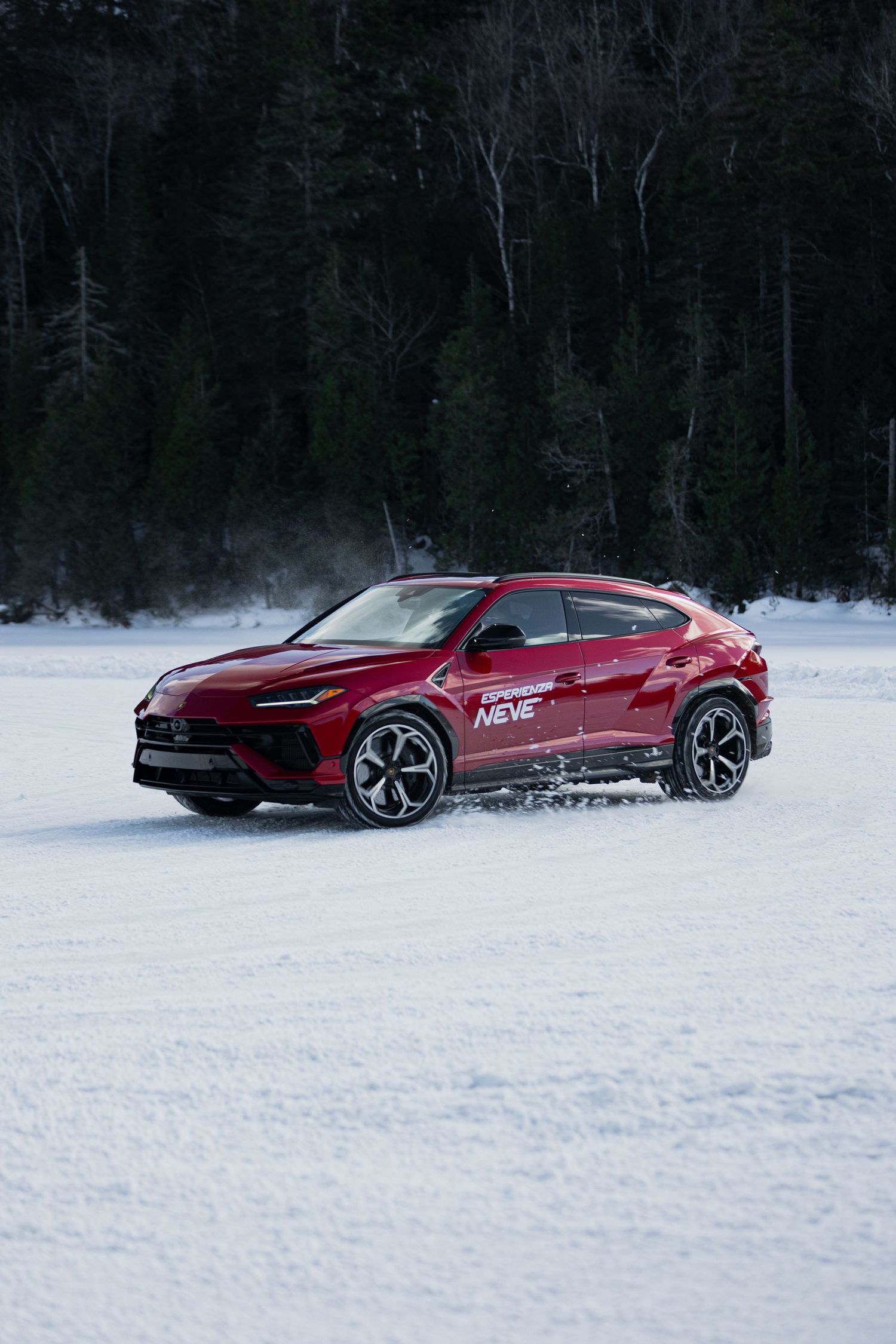 A red Ferrari sports car drifting and sliding through snowy terrain on a winter test track.