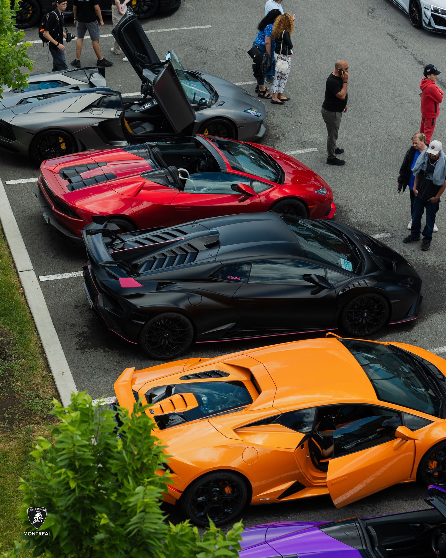 A lineup of exotic supercars including Lamborghinis in vibrant orange, red and black colors parked at an outdoor event.