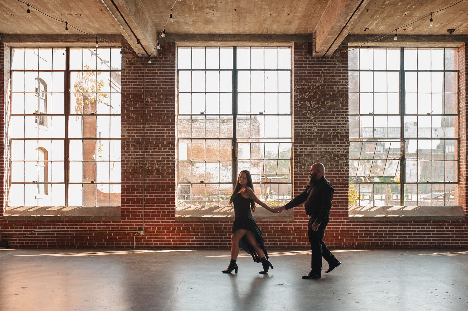 Couple holding hands walking through dye room at industrial Lindale Mill in NW GA for edgy cinematic dark engagement session.