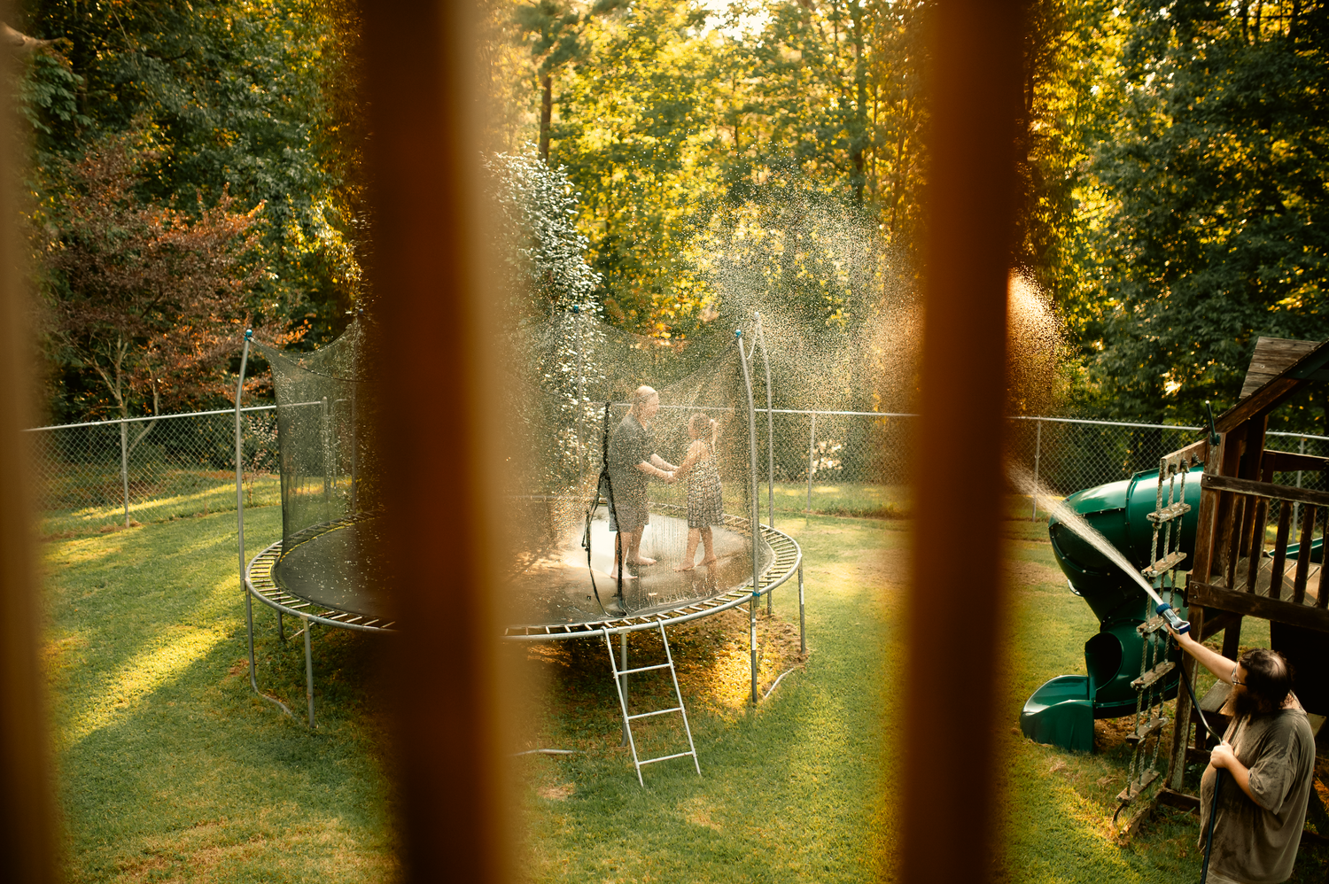 Dad squirting kids with water hose on trampoline for lifestyle family photography session in Cartersville, GA.