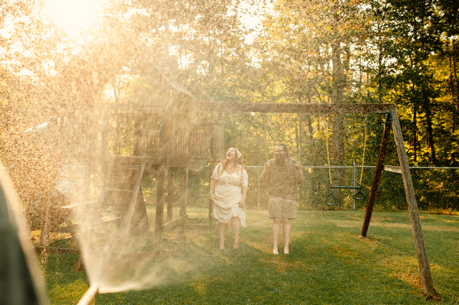 Mom and dad laughing with water hose on swingset for family photos in Cartersville, GA.