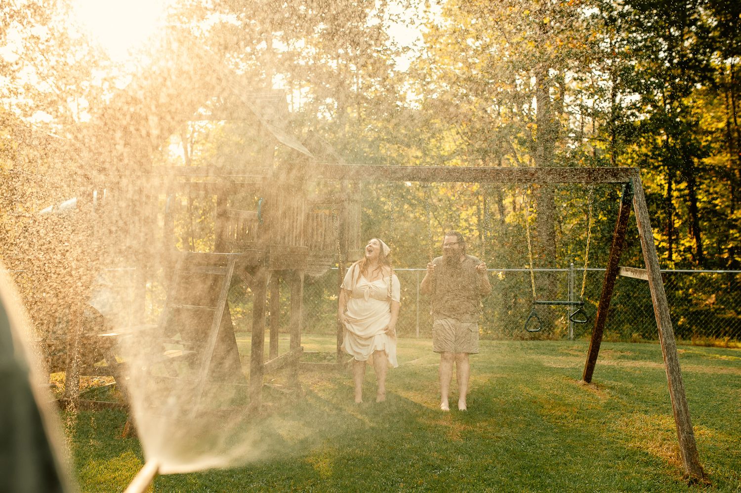 Mom and dad laughing with water hose on swingset for family photos in Cartersville, GA.