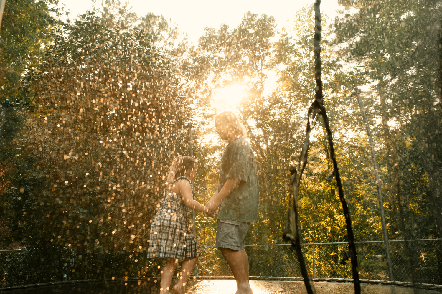 Son and daughter playing in water hose rain on trampoline in family photos in Cartersville, GA.