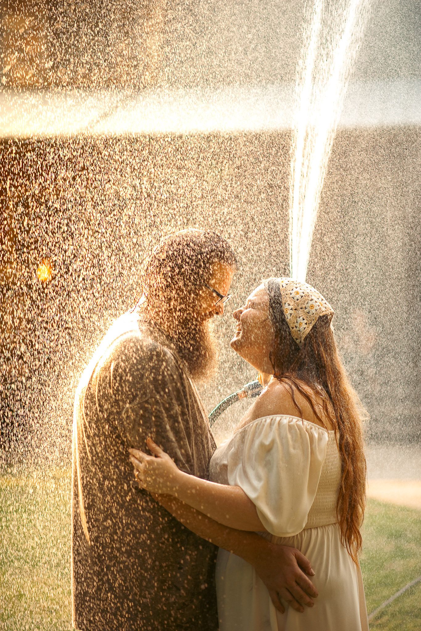 Husband and wife holding each other smiling under water hose in family photos in Cartersville, GA.