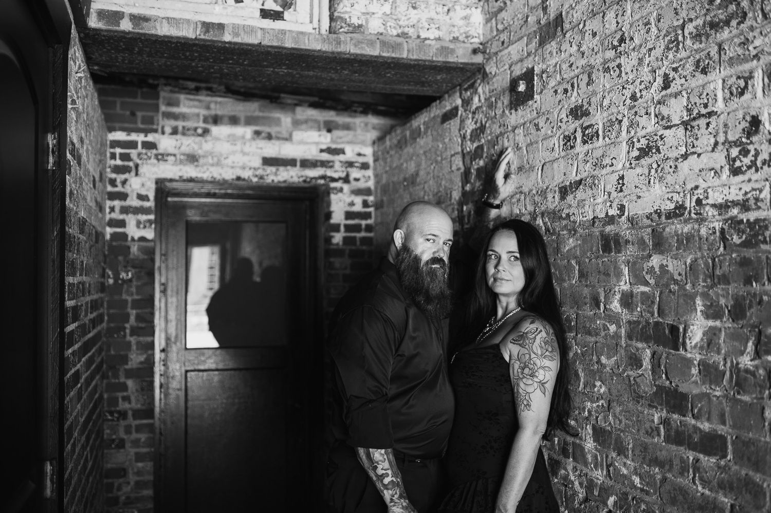 Couple leaning against brick wall in edgy tattooed engagement session at Lindale Mill in Rome, GA.