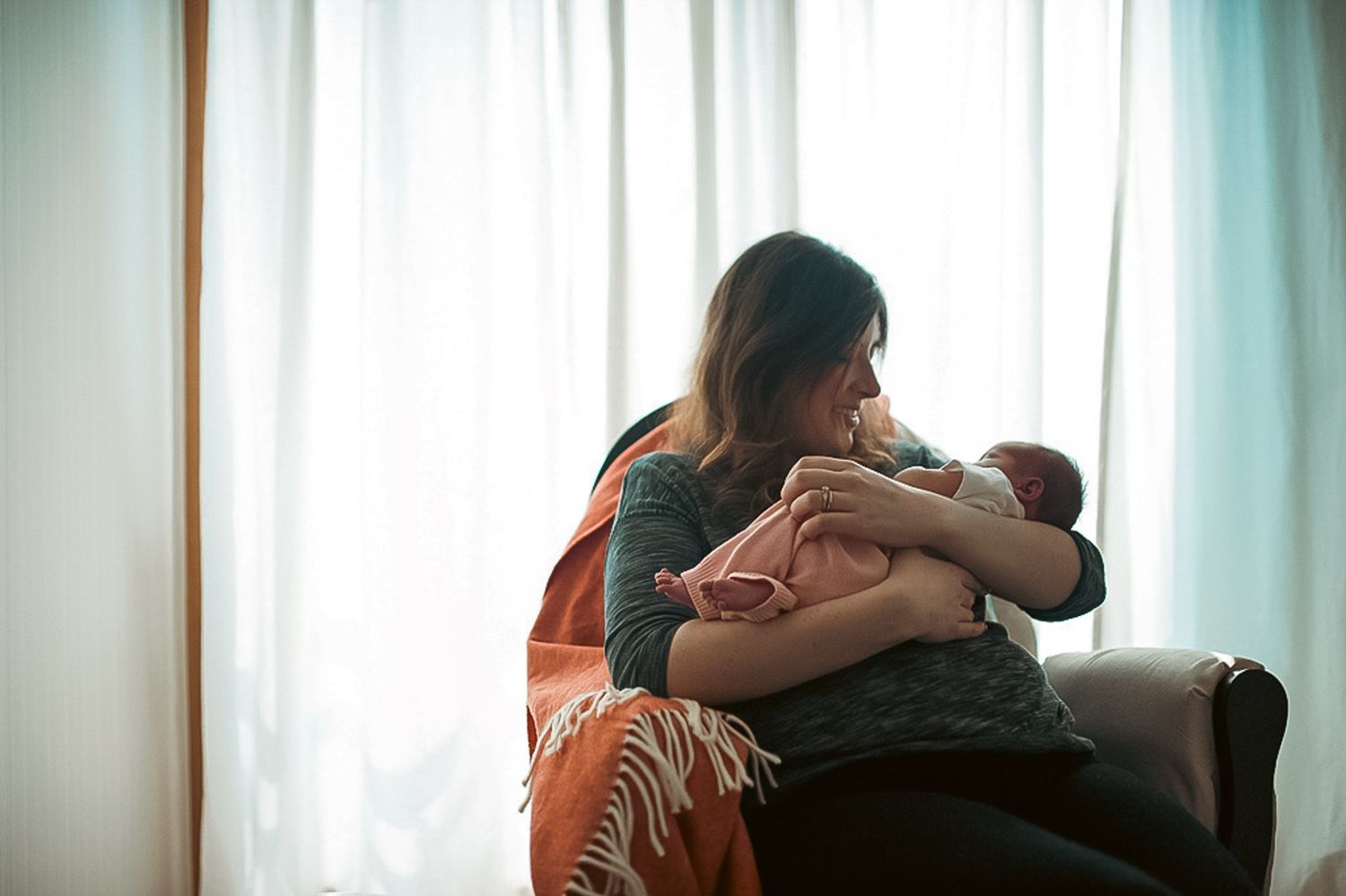 Mom rocking baby in front of window in at home newborn session in Acworth, GA.