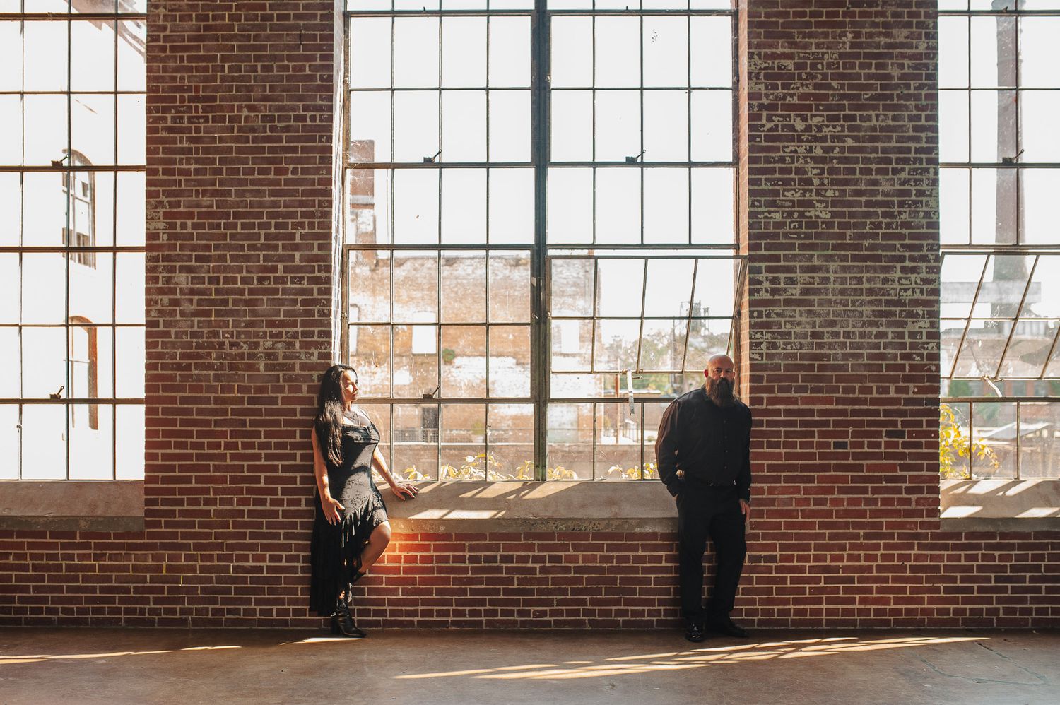 Couple standing on opposite sides of the window for interesting cinematic engagement portrait in Lindale Mill.