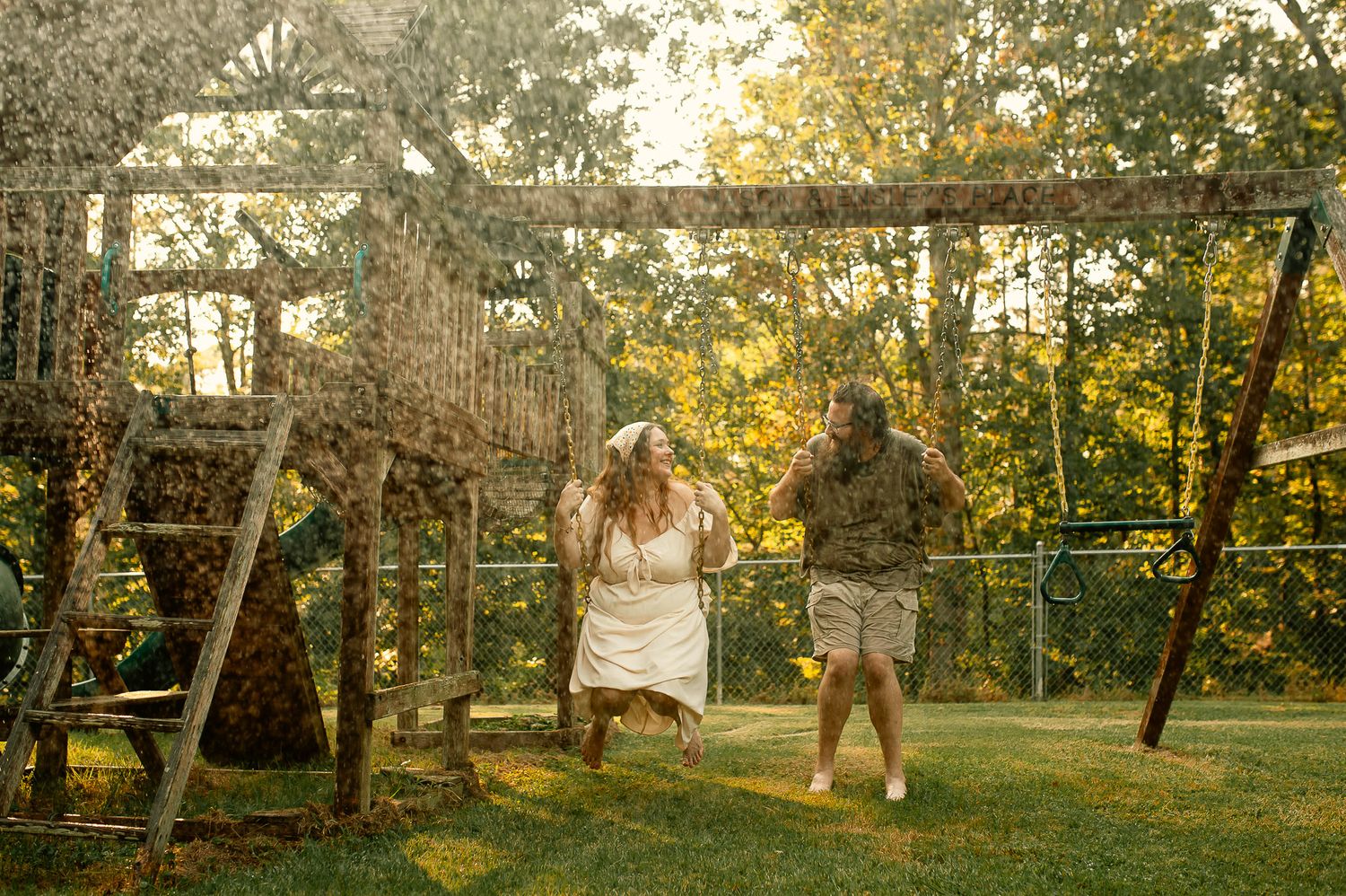 Mom and dad laughing with water hose on swingset for family photos in Cartersville, GA.
