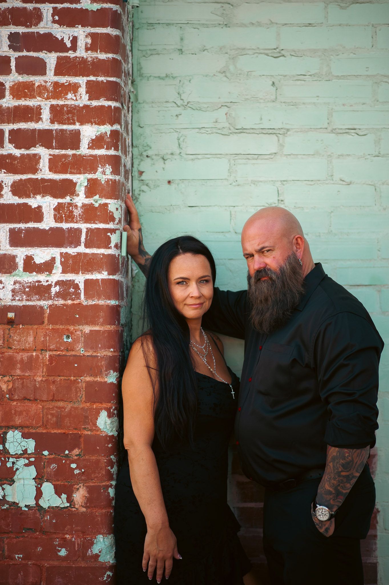 Couple posing in front of painted brick wall for moody engagement session in Lindale Mill's outdoor industrial ruins.