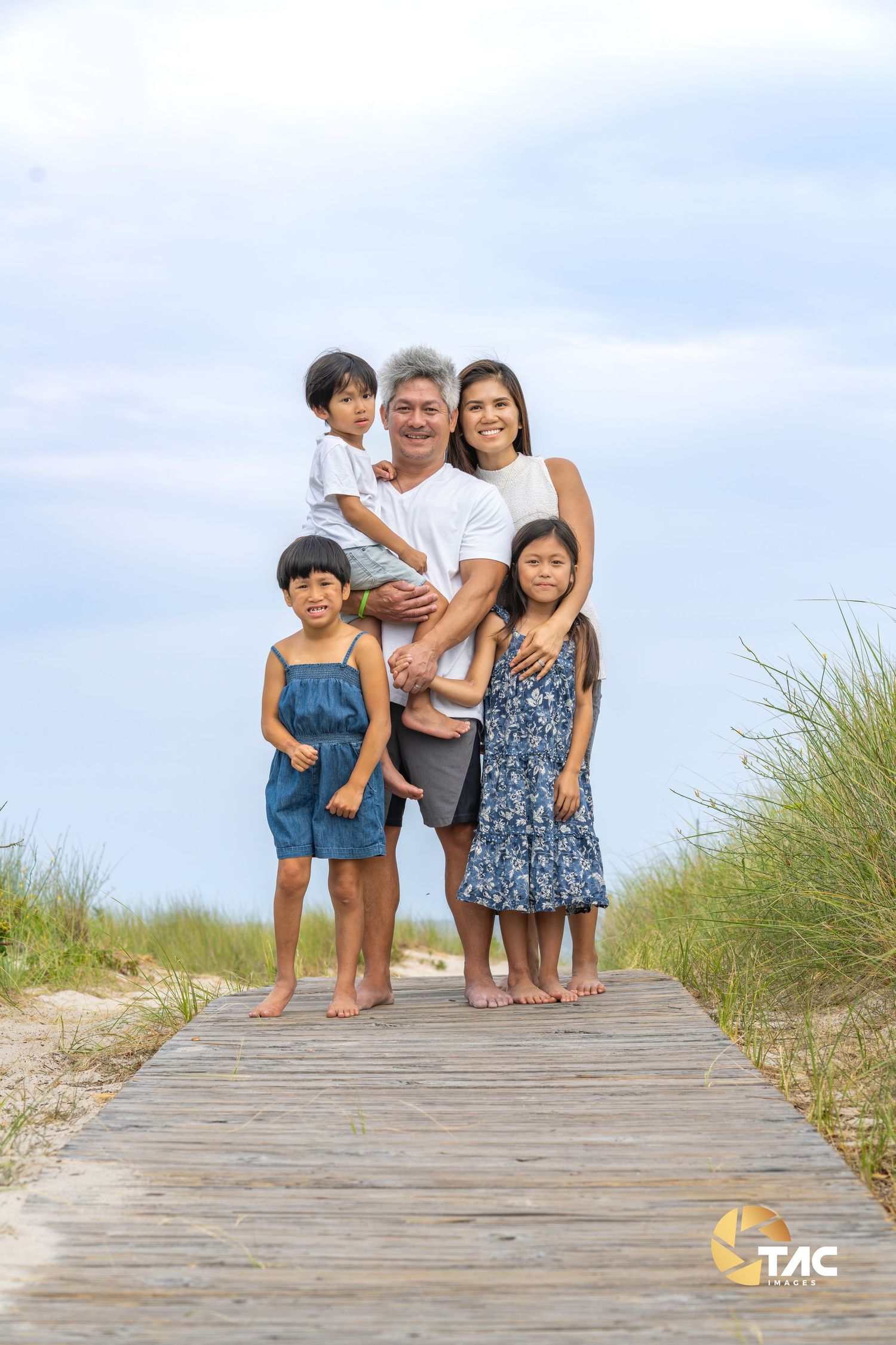 Family photoshoot on a wooden boardwalk at the beach with natural scenery.