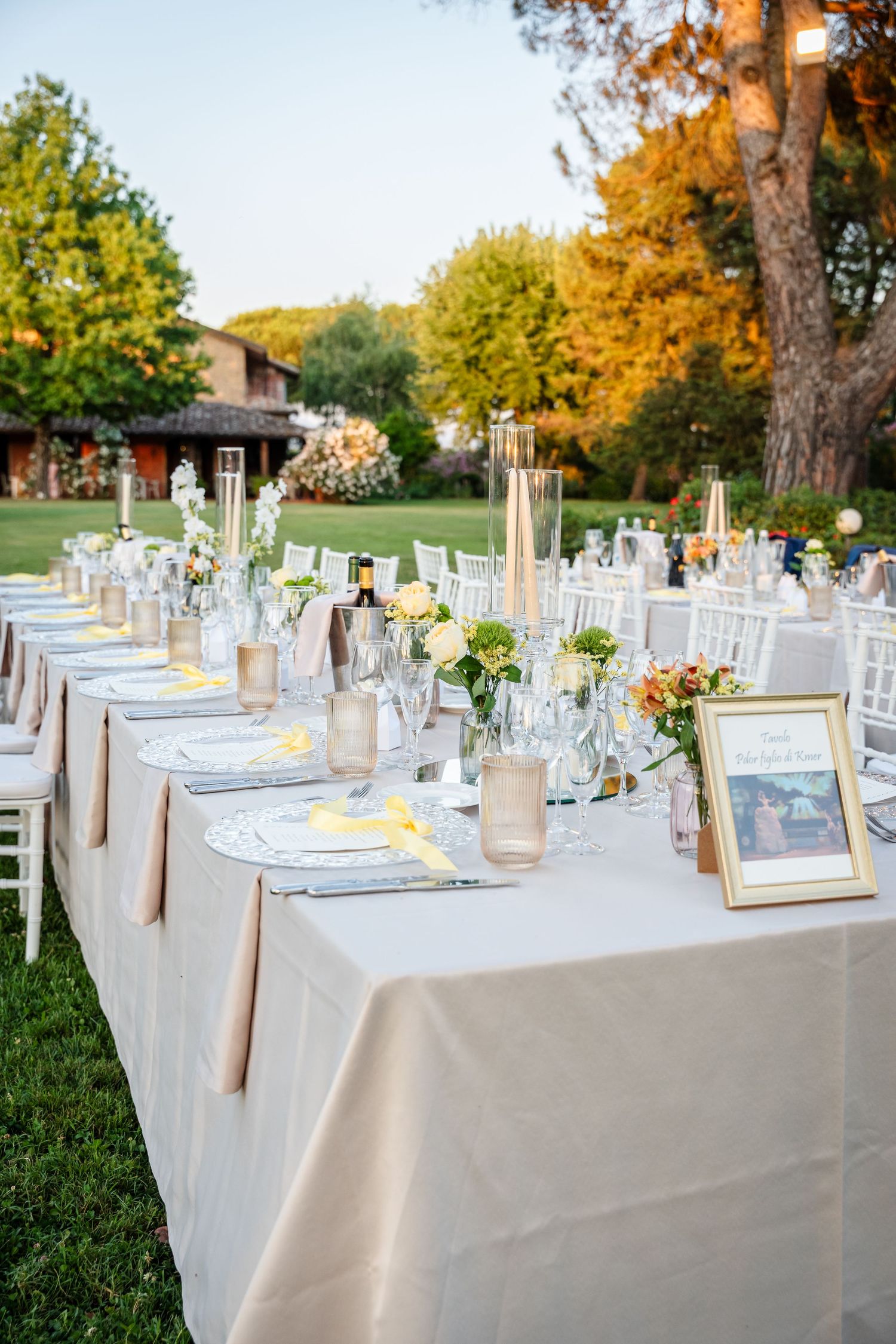Elegant outdoor wedding reception table set with floral centerpieces, candles, and white linens in a garden setting.