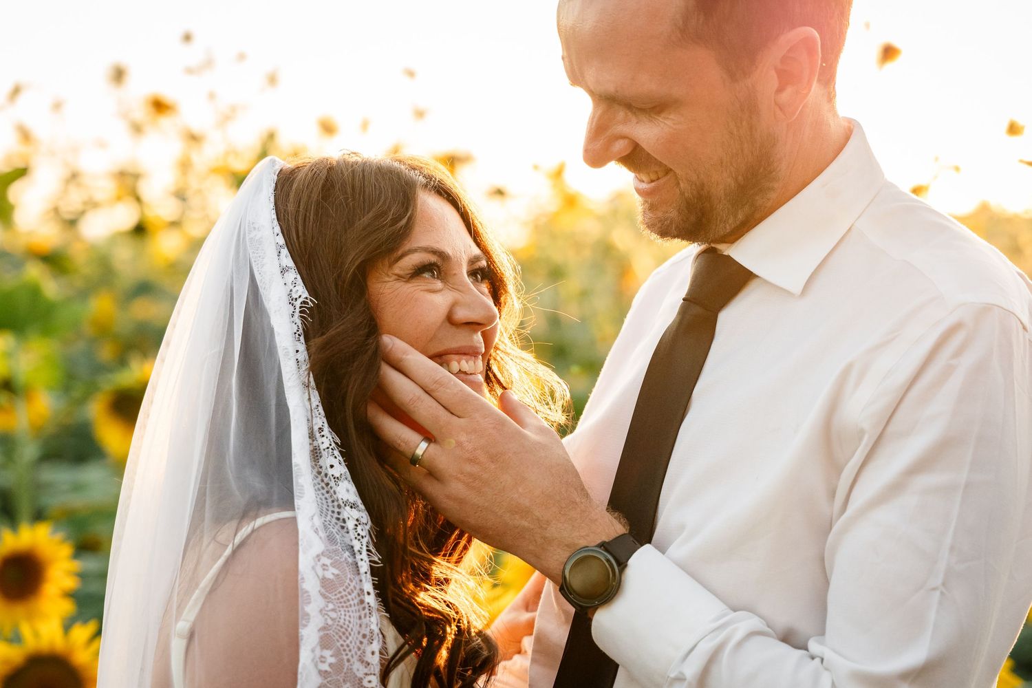 Groom gently holds bride's face as they share an intimate moment in a sunflower field.