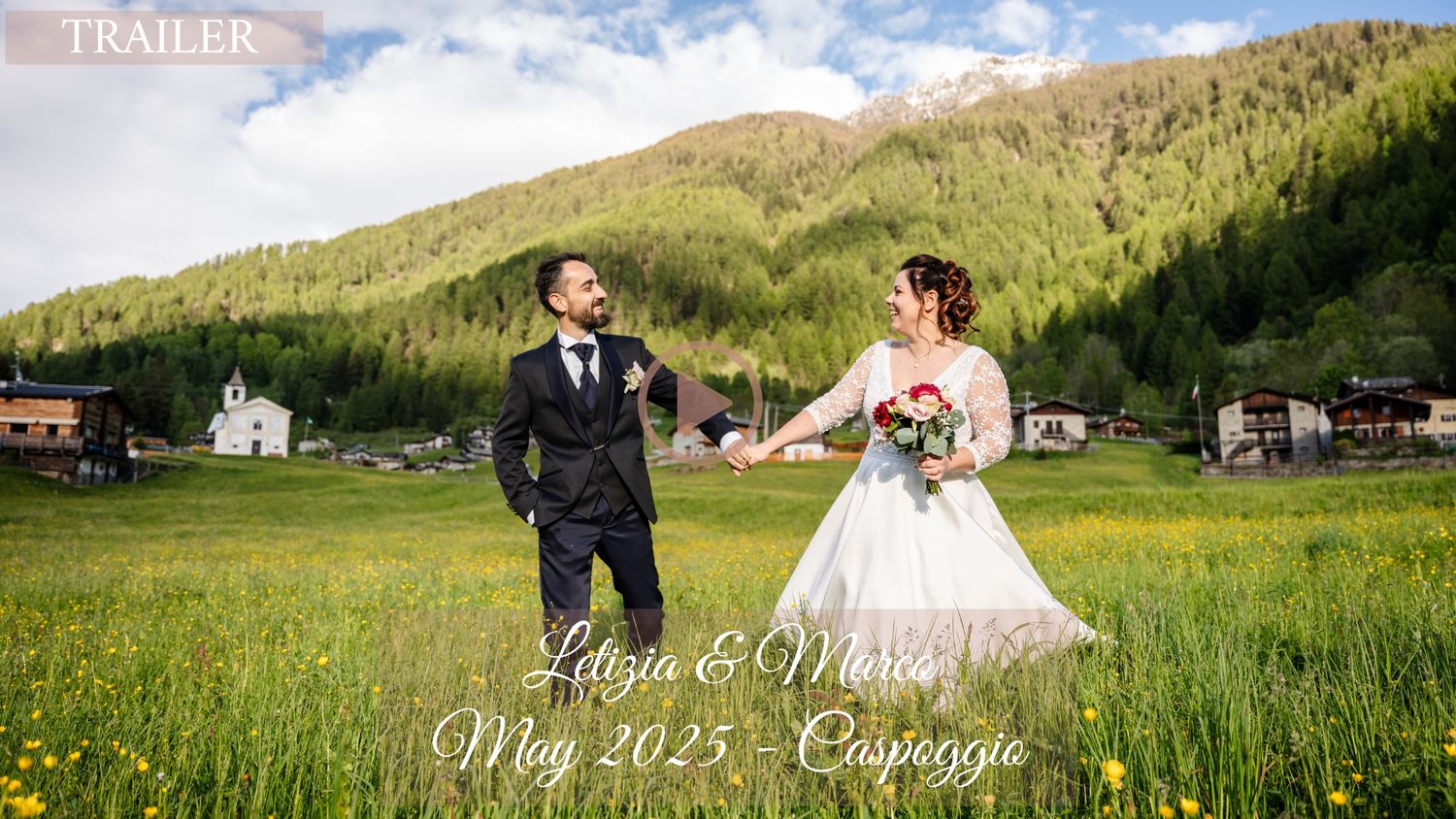 A couple celebrates their wedding in a scenic mountain meadow with rustic buildings in the background.