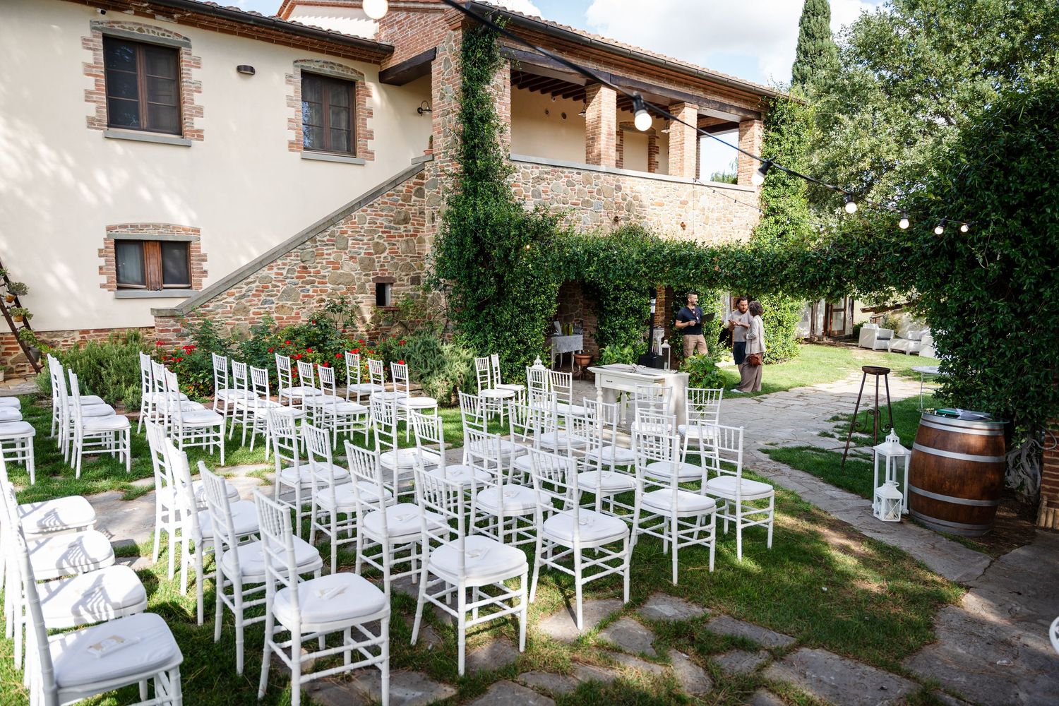 Panoramic view of white wooden chairs arranged for an outdoor wedding ceremony in a rustic garden setting.