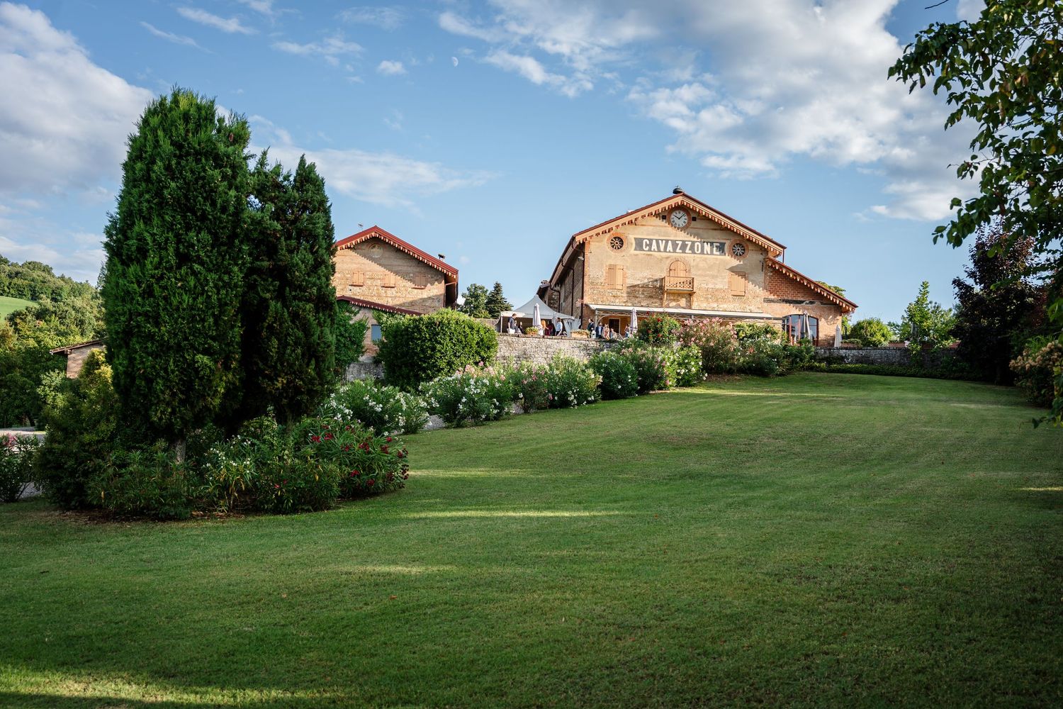 Elegant wooden wedding venue surrounded by lush green gardens and manicured lawns under a blue sky.
