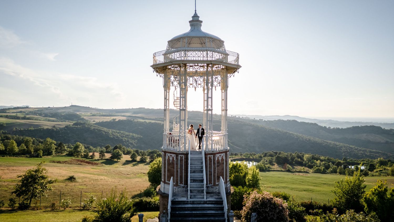 Wedding couple standing in elegant gazebo with scenic countryside views.