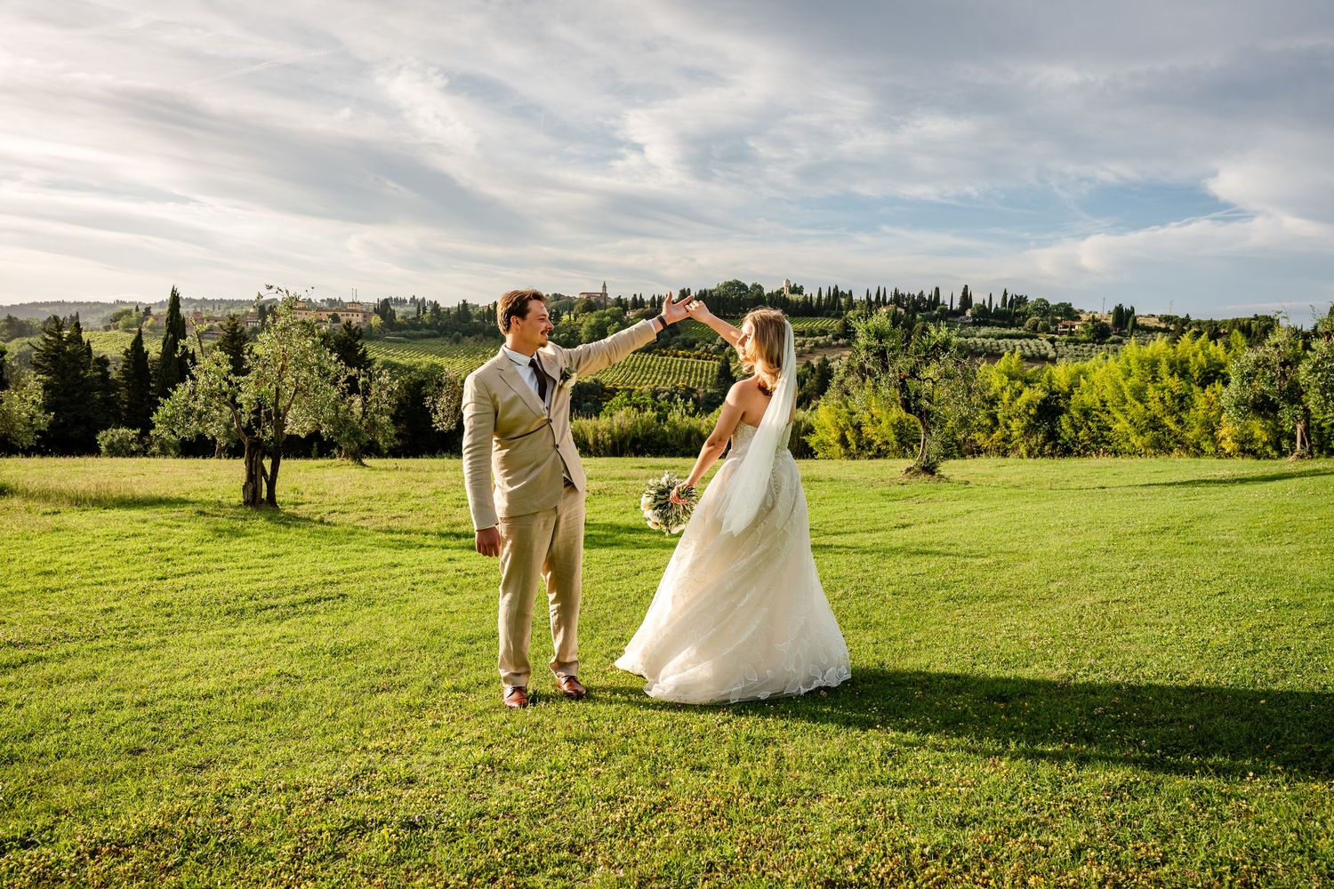 Bride and groom dancing on green lawn with Tuscan countryside backdrop on their wedding day.