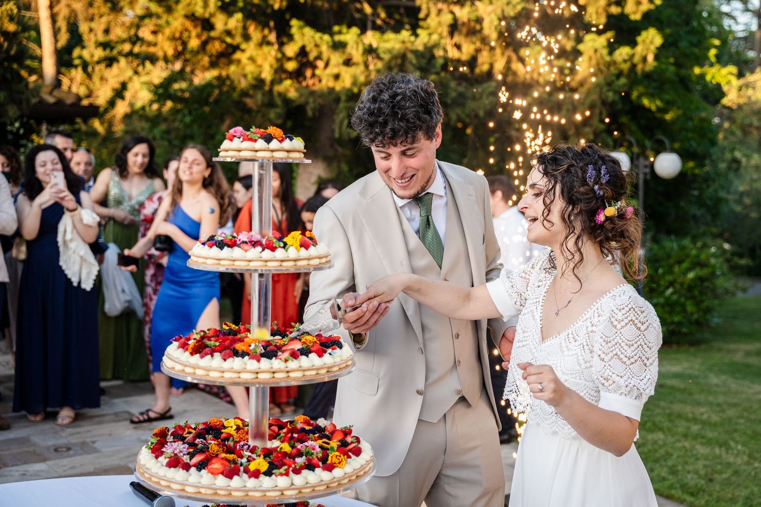 Wedding couple cutting their colorful fruit-topped wedding cake at an outdoor garden reception celebration.