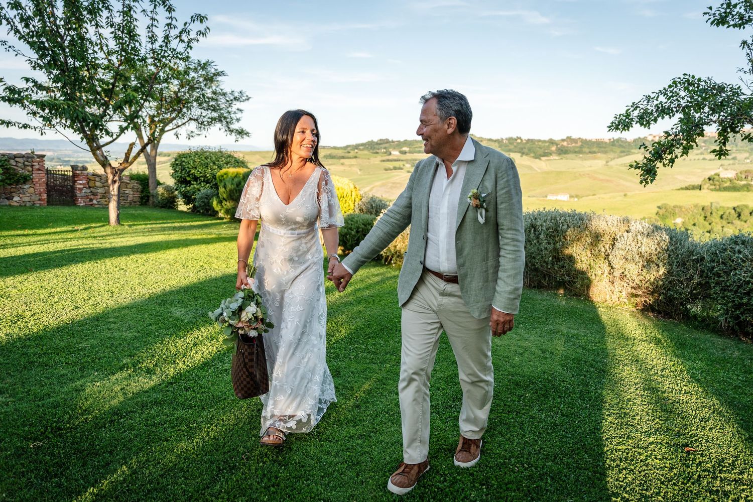 Couple walking hand in hand through a sunny meadow during golden hour in a romantic outdoor setting.