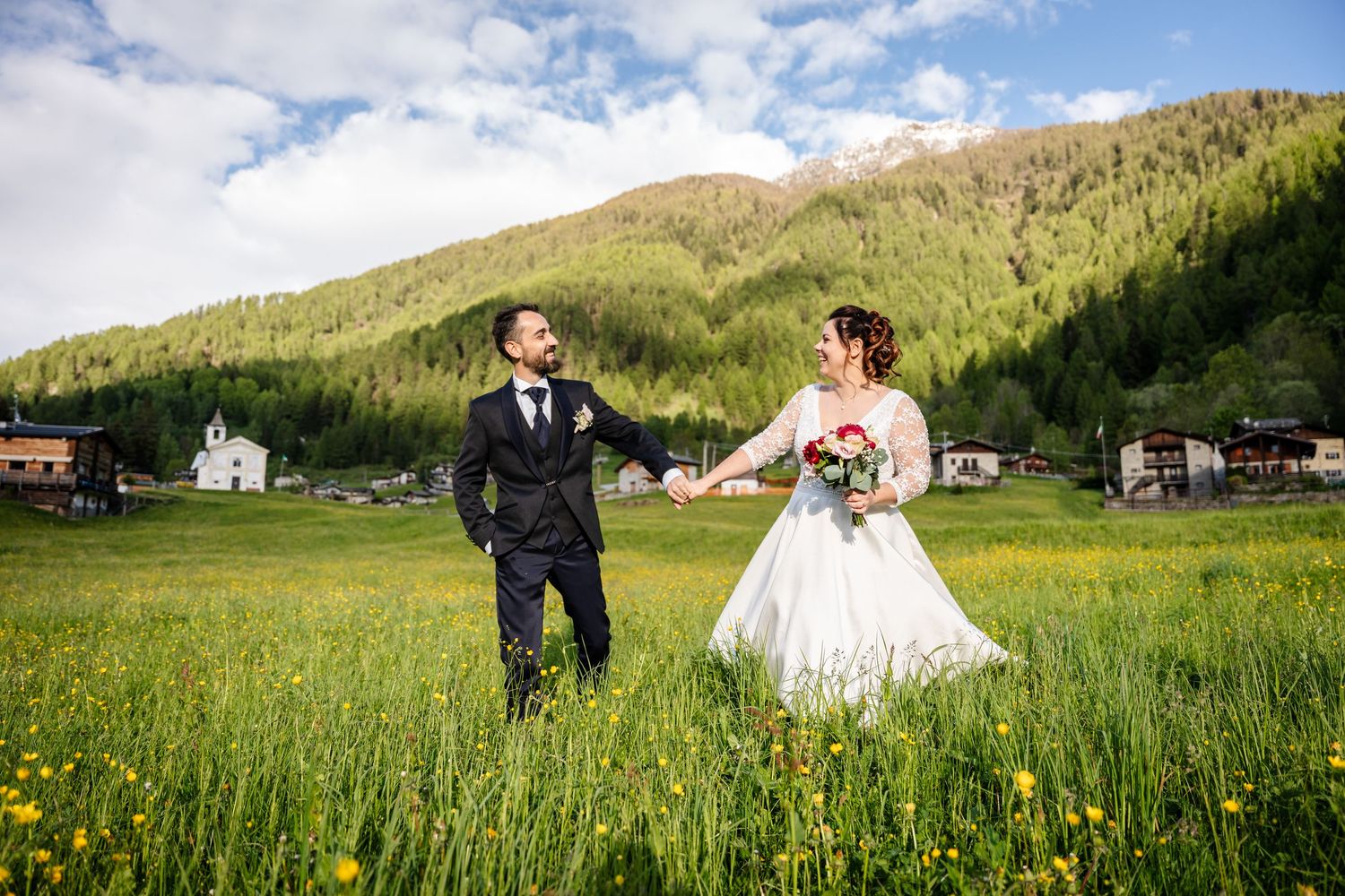 Wedding couple stands in a scenic mountain meadow filled with wildflowers on a sunny summer day.