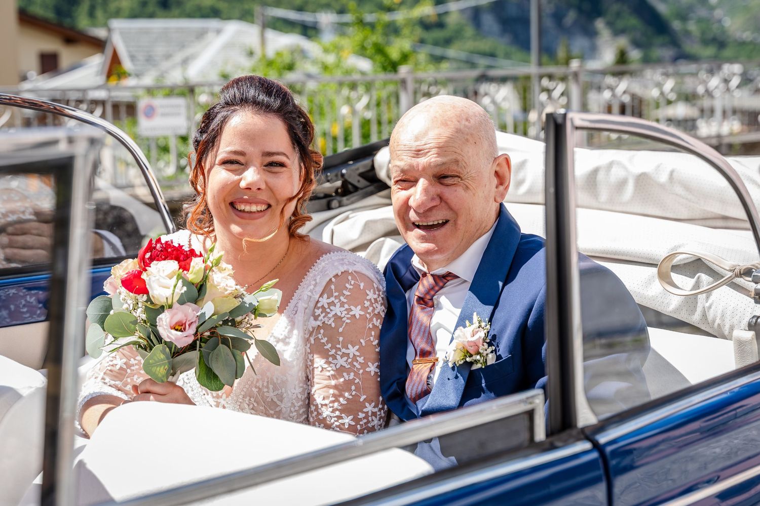 Smiling couple sitting in a vintage car decorated with flowers for a wedding celebration.