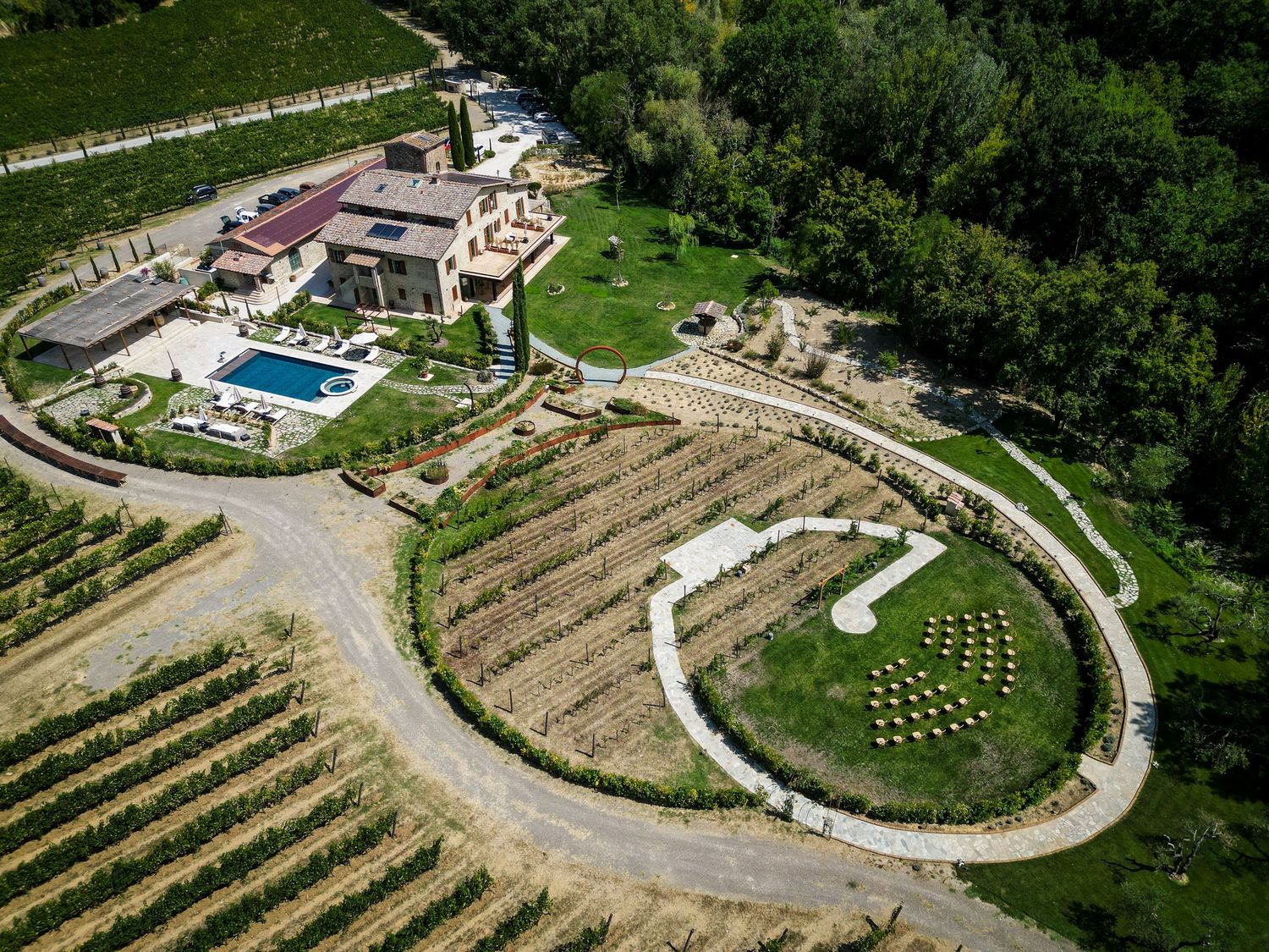 Aerial view of a luxury vineyard estate with a pool, circular garden feature, and lush green vines in a scenic countryside.