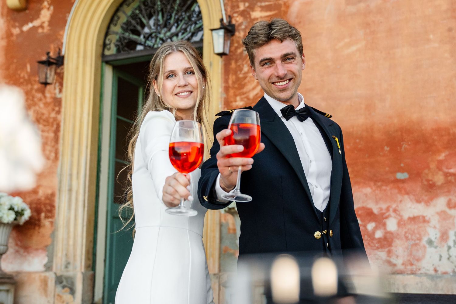 Bride and groom toasting with red wine glasses outdoors at elegant venue on wedding day.