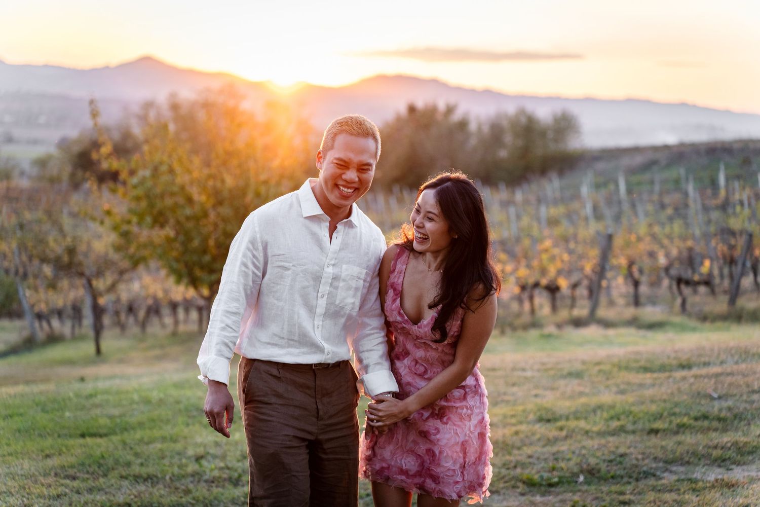 A couple shares a romantic moment in a vineyard at sunset while wine tasting among the grapevines.
