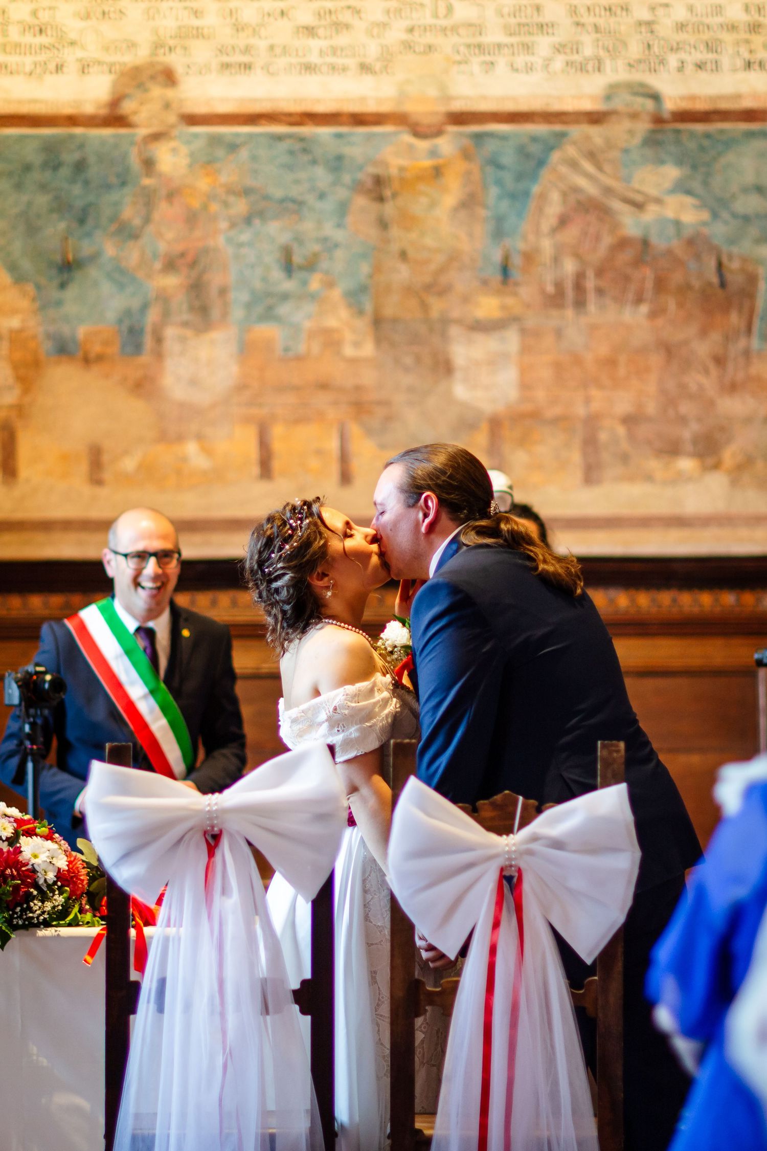 Bride and groom share their first kiss at a civil wedding ceremony in a historic Italian hall.