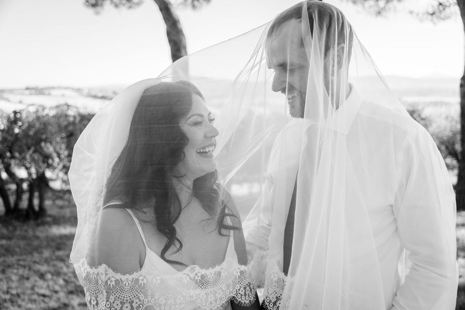 Black and white portrait of laughing bride and groom sharing a joyful moment under her veil.