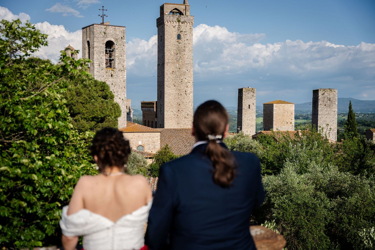 Wedding couple views medieval towers of San Gimignano, Italy from scenic overlook on their wedding day.