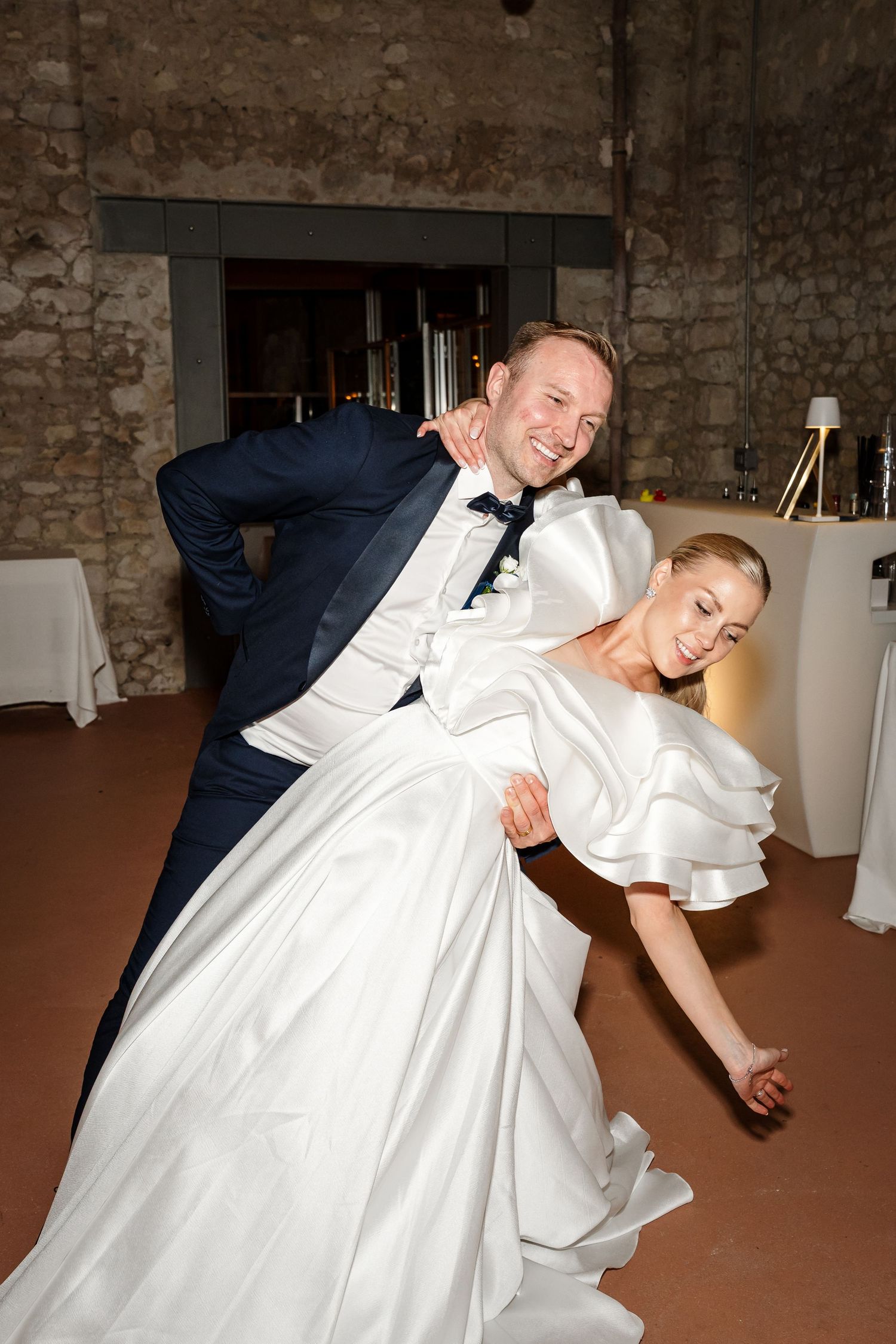 A sequence of dance moves shows a couple performing a dramatic dip during a wedding celebration on a rustic dance floor.