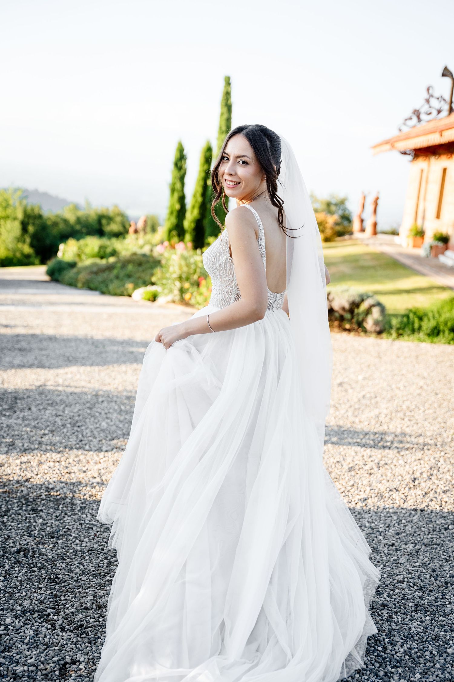 A flowing white wedding dress twirls gracefully on a gravel path during golden hour at an outdoor venue.
