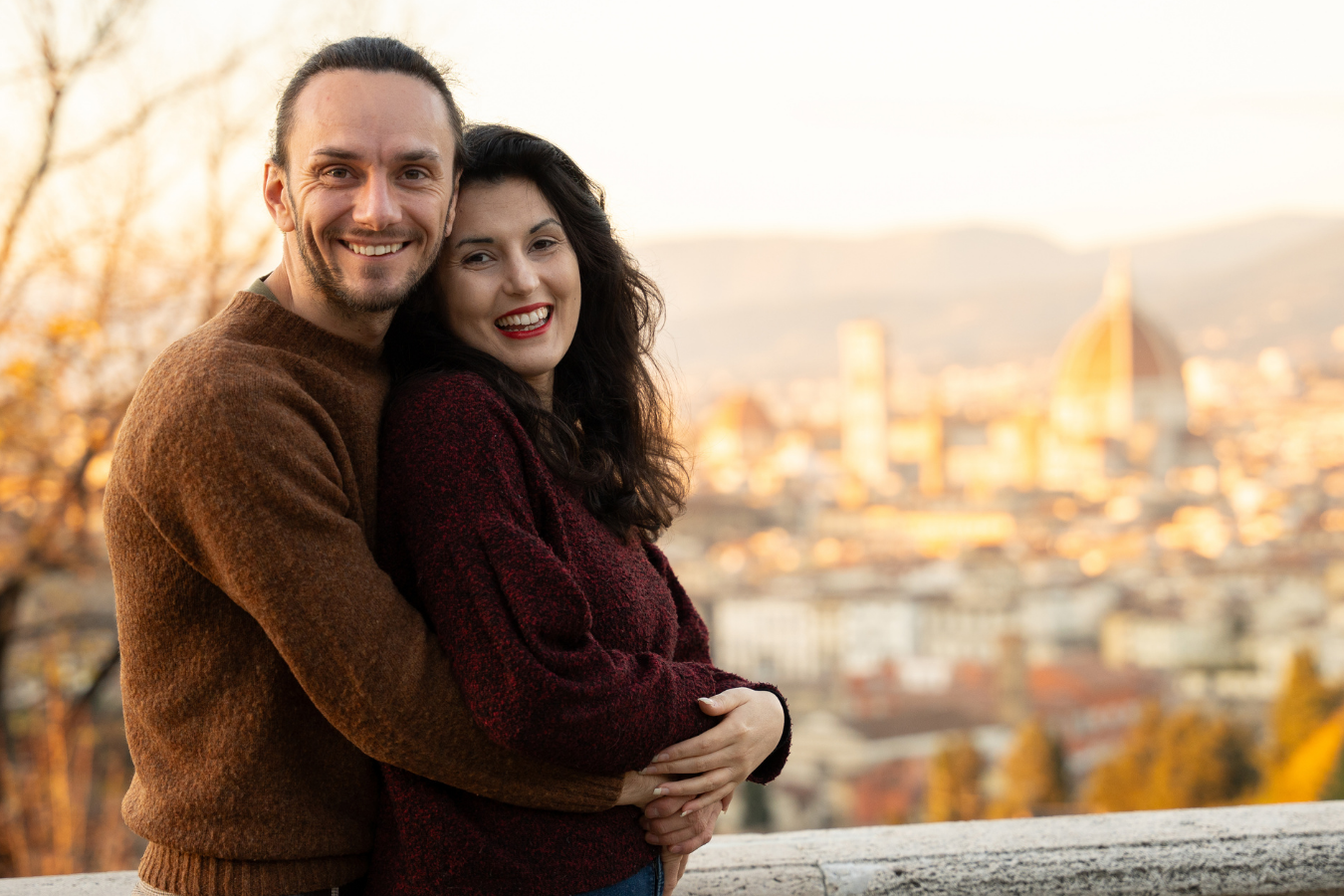 A couple embraces while enjoying a scenic autumn sunset view overlooking a city landscape.