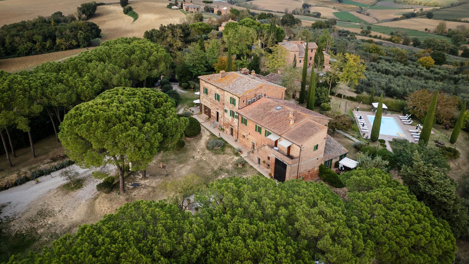 Aerial panoramic view of a rustic villa surrounded by lush gardens and rolling countryside in Tuscany.